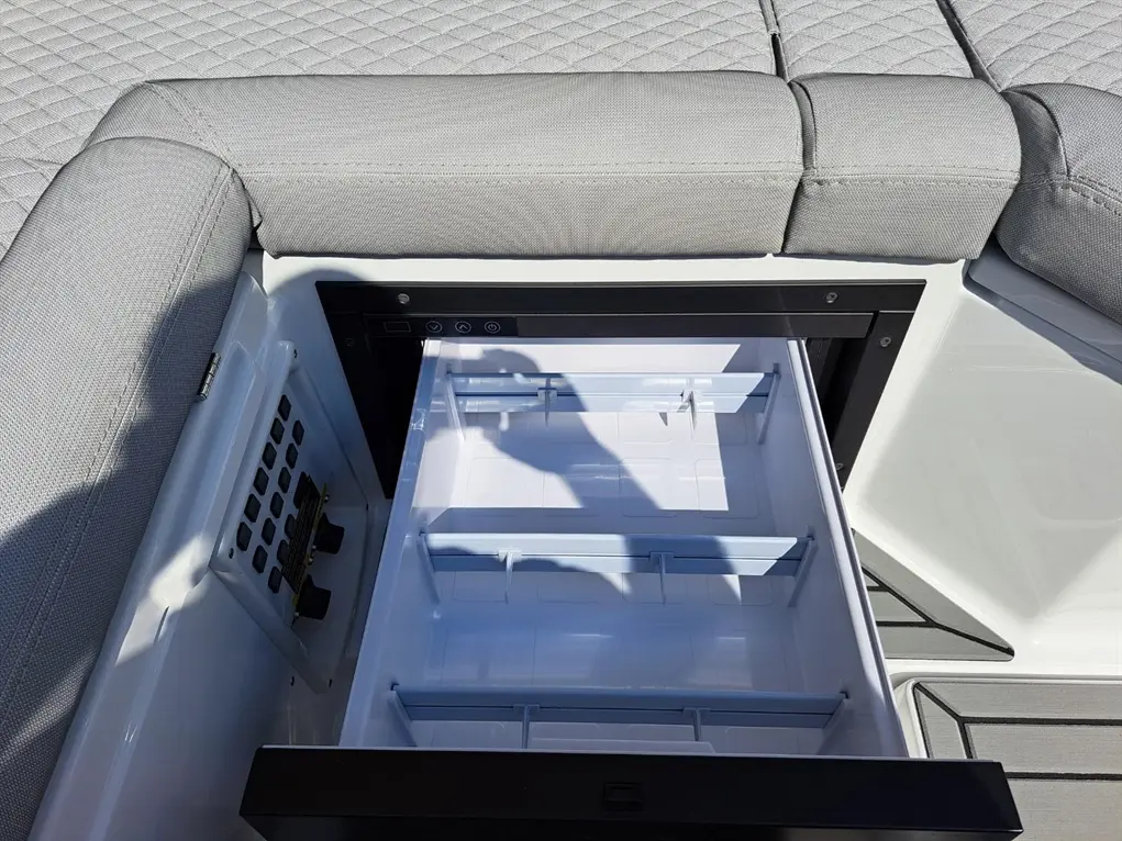 A modern boat storage compartment with an open drawer revealing empty shelves, grey upholstery, and control panel nearby.